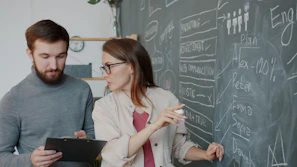 Two colleagues discussing a plan on a chalkboard.