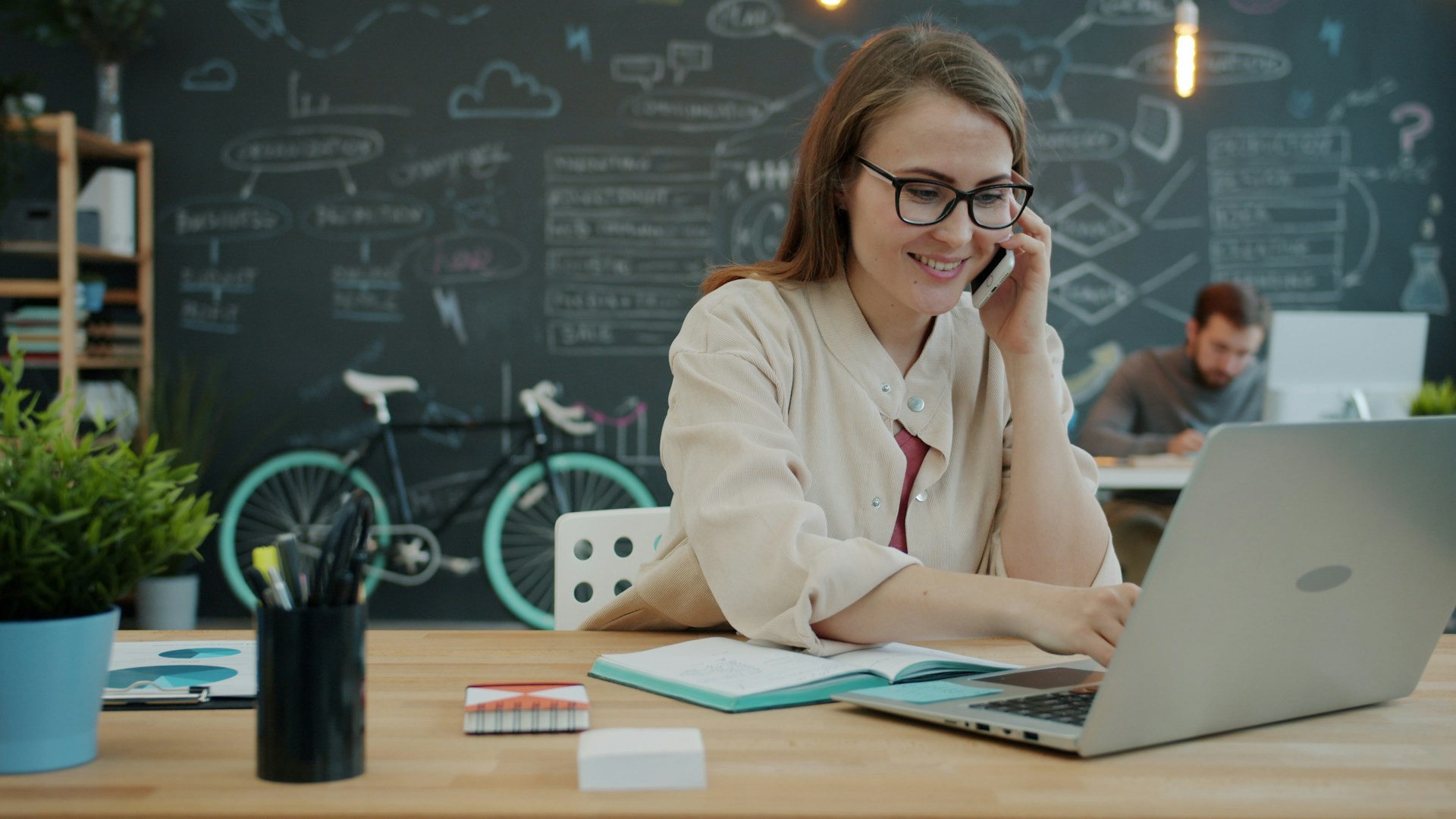 Woman talking on phone while working on laptop in office