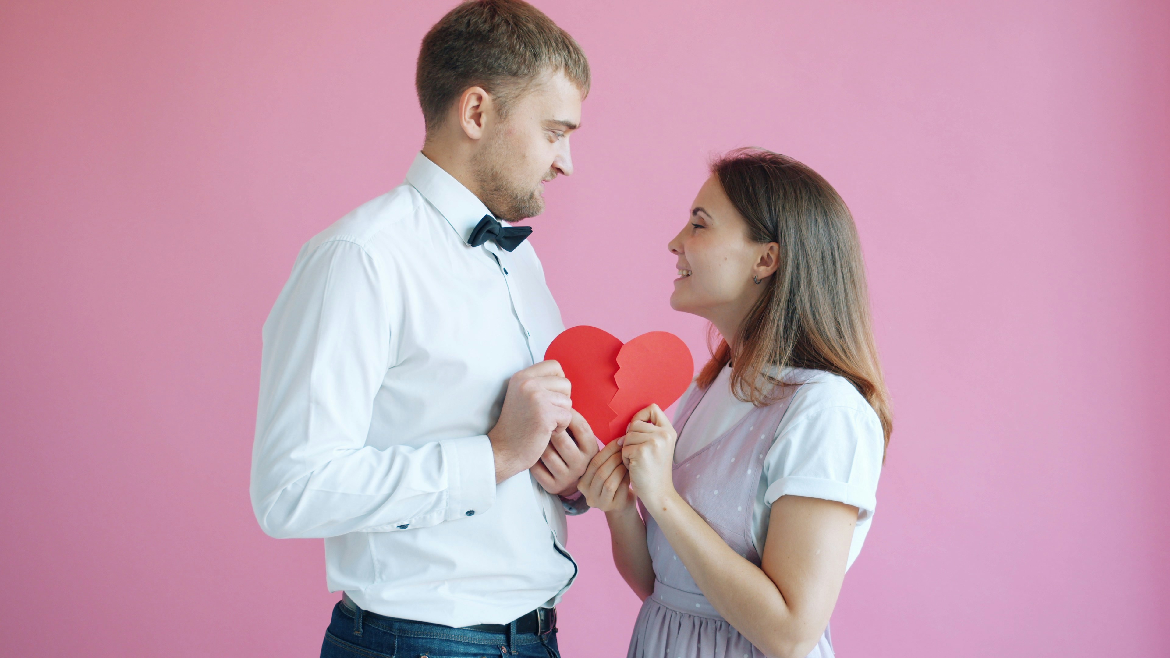 Couple holding a broken heart on pink background