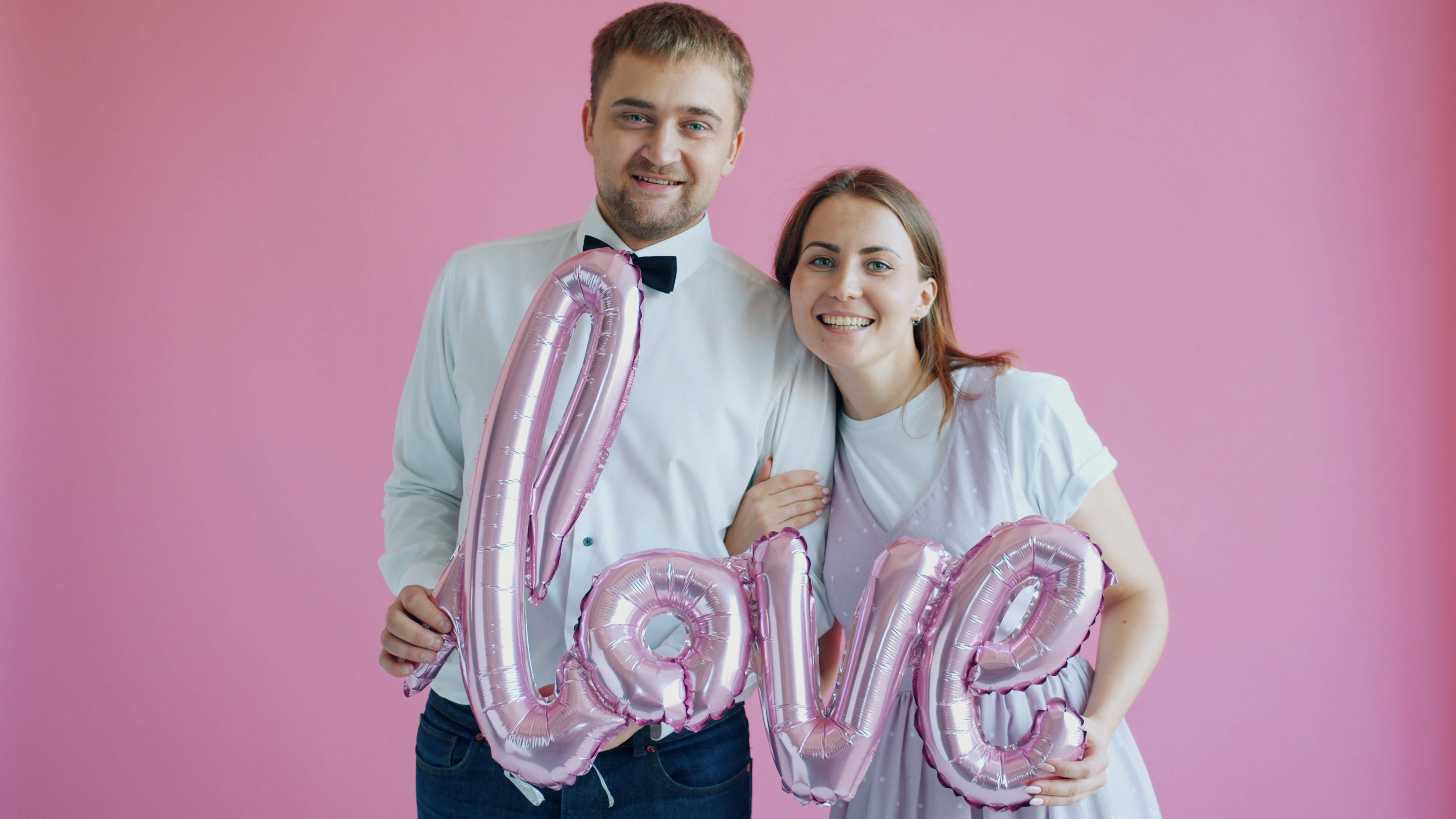Couple holding pink 'love' balloons on pink background