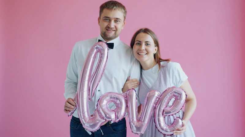 couple holding love balloons on a pink background