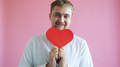 Man holding a red heart against pink background
