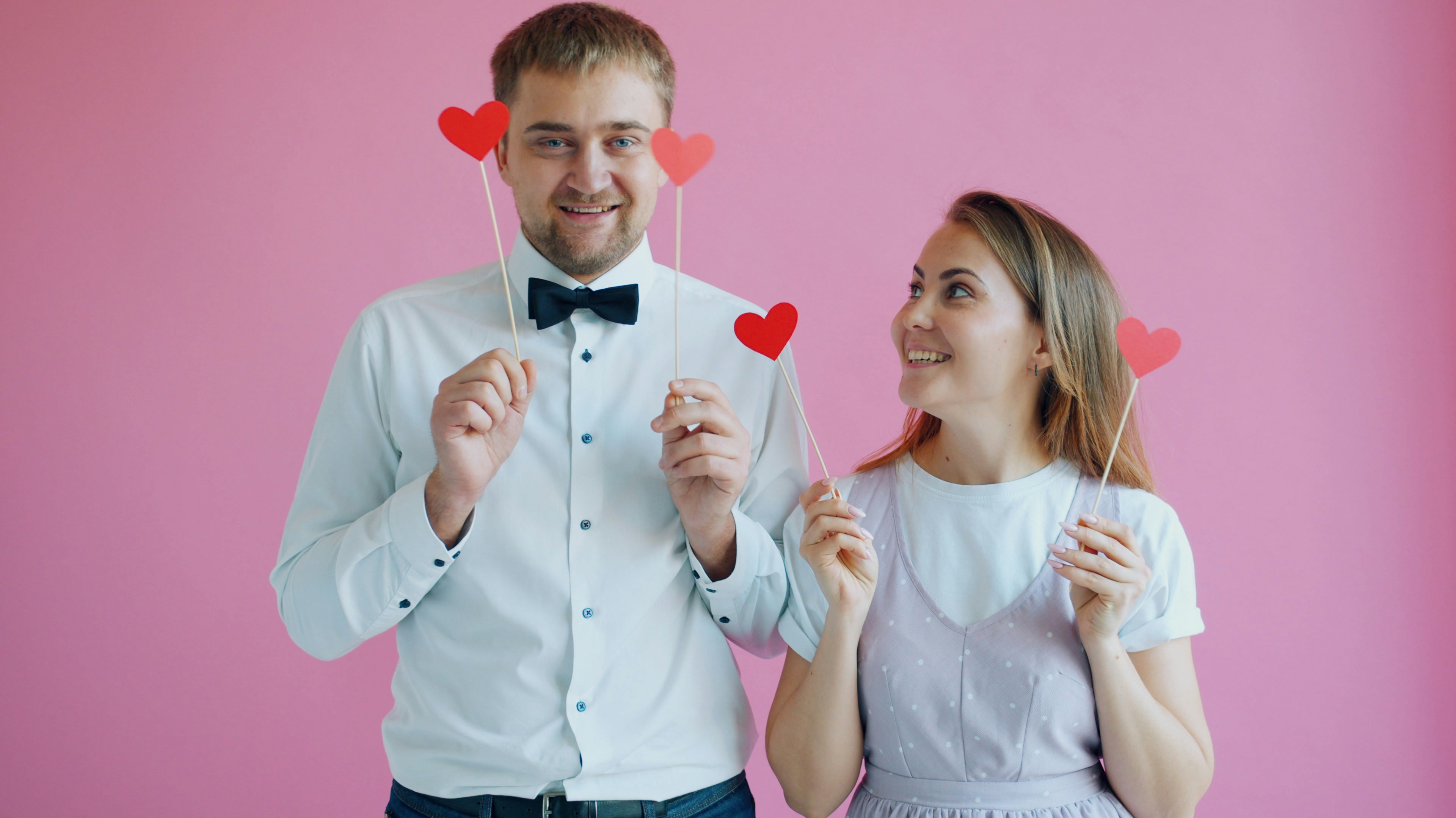 Happy youth girl and guy are holding hearts hiding eyes laughing enjoying romance on valentine's day. Closeness, feelings and positive emotions concept.