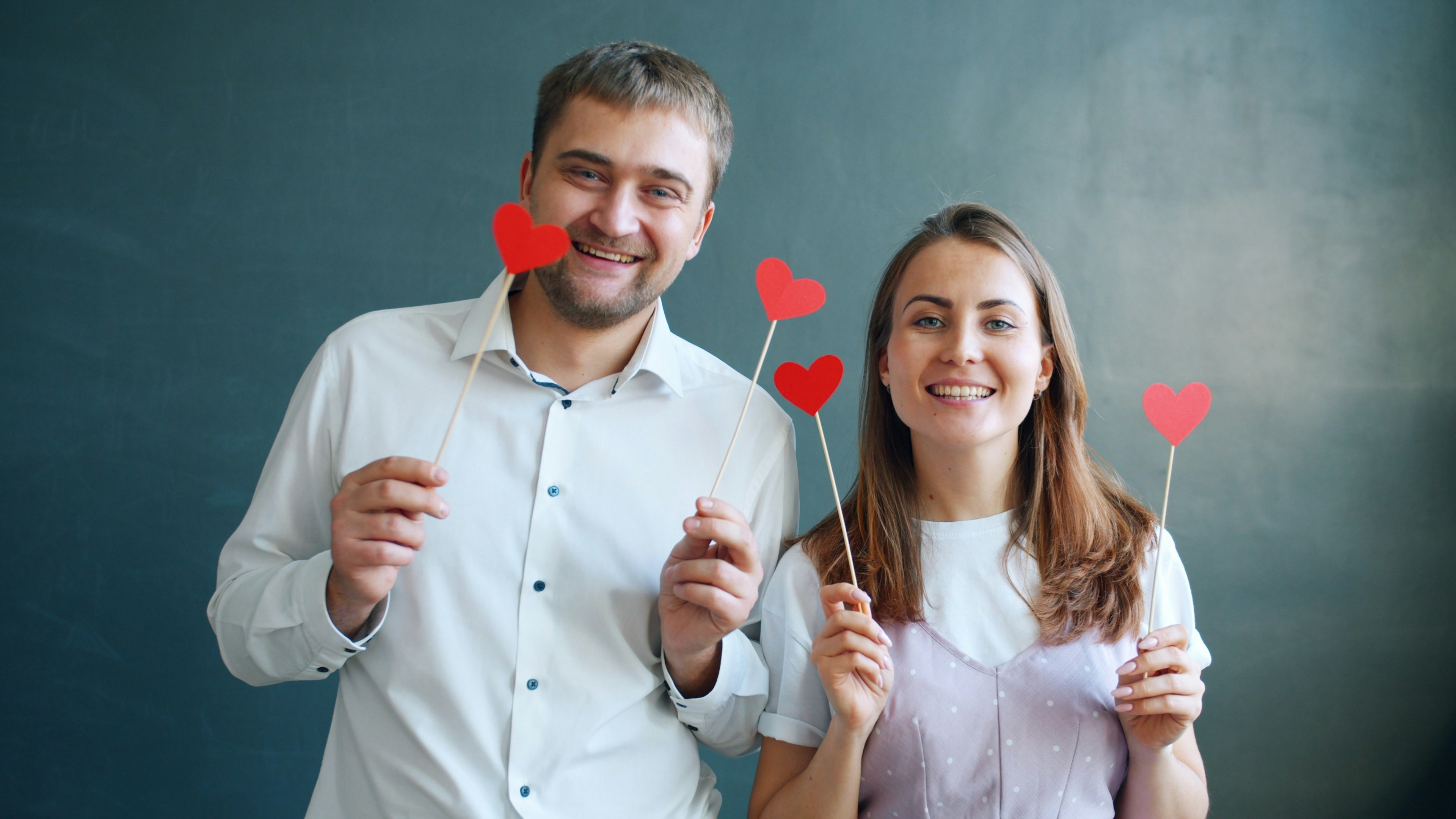 Playful heterosexual couple holding hearts moving hands smiling feeling happy on Valentine's day together. Lifestyle, youth and celebrations concept.