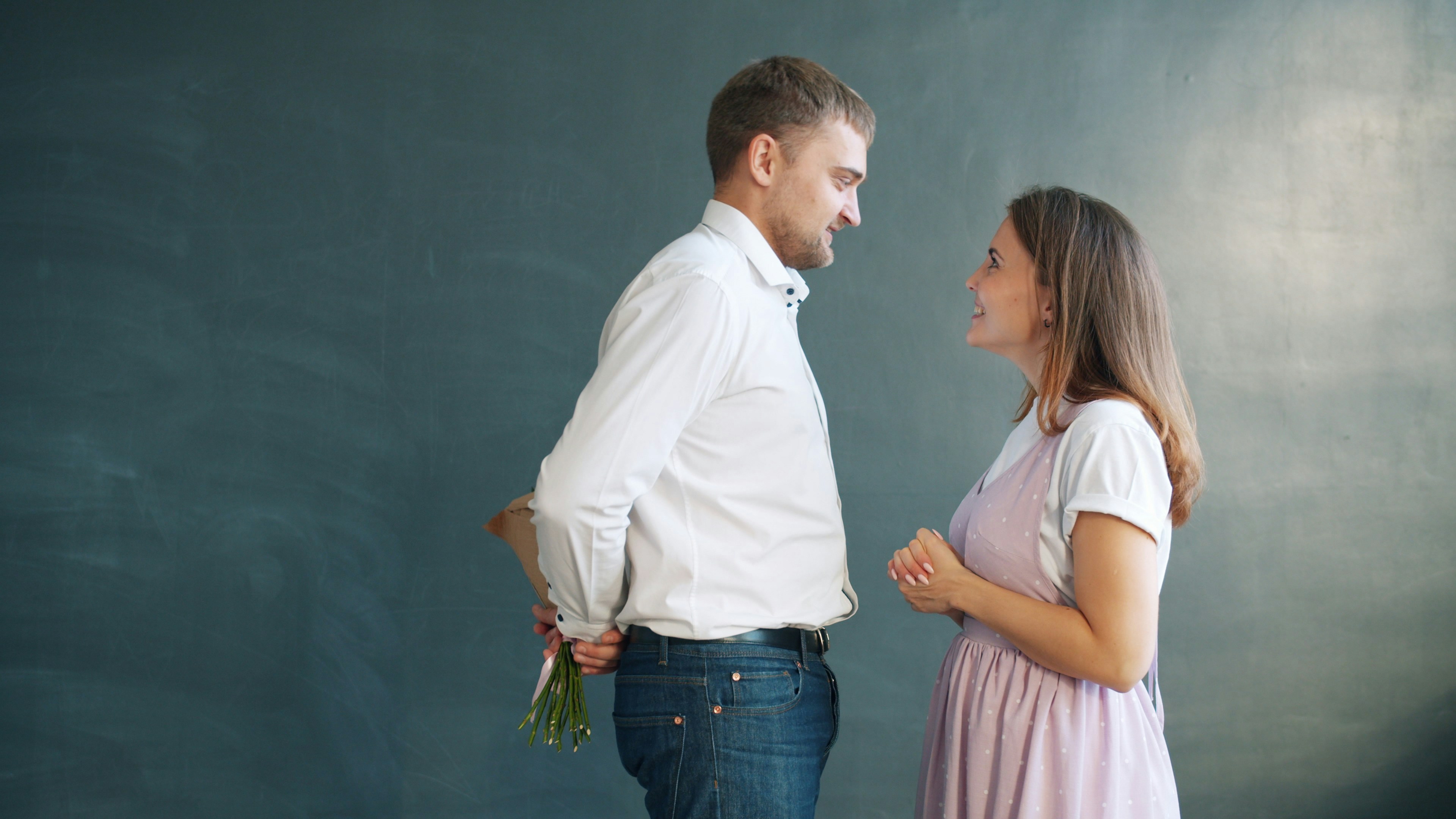 Attractive bearded guy is giving bunch of flowers to surprised girl kissing smiling making young woman happy and excited. People and romance concept.