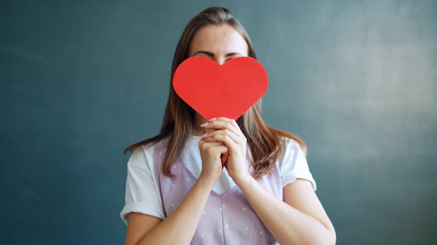 Woman holding a red heart in front of her face.
