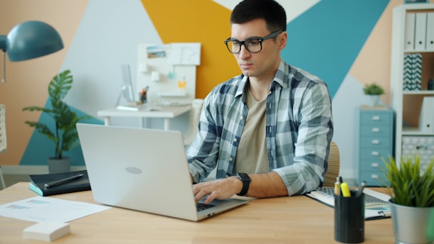 Man wearing glasses types on a laptop at a desk.