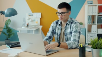 Man wearing glasses typing on a laptop at a desk.