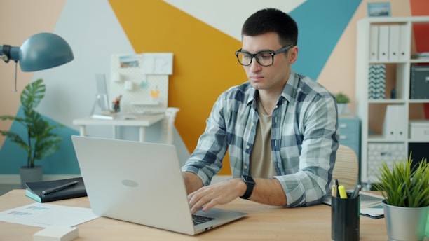 Man wearing glasses typing on a laptop at a desk.