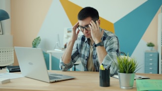 Man holding head in frustration at desk with laptop.