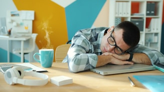 Man sleeping at desk with coffee and laptop.
