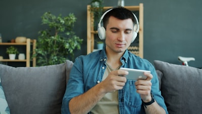 Man wearing headphones plays game on smartphone.