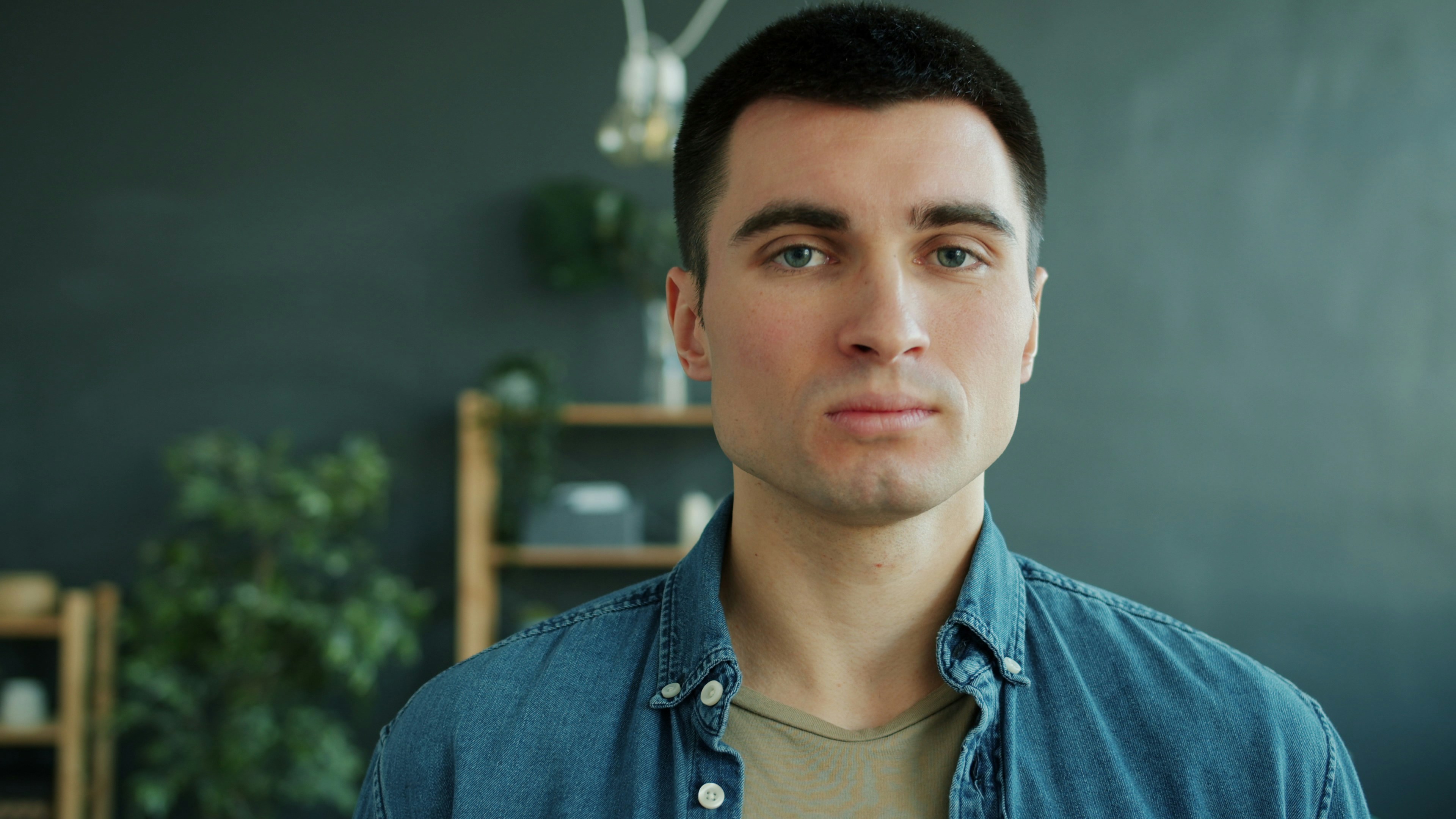 Slow motion of handsome guy with serious face smiling standing alone indoors in apartment and looking at camera changing facial expression. Human emotions and people concept.