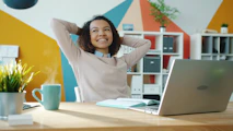 Woman relaxing at desk with laptop and coffee.
