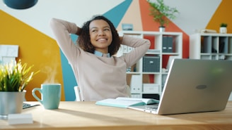 Woman relaxing at desk with laptop and coffee.