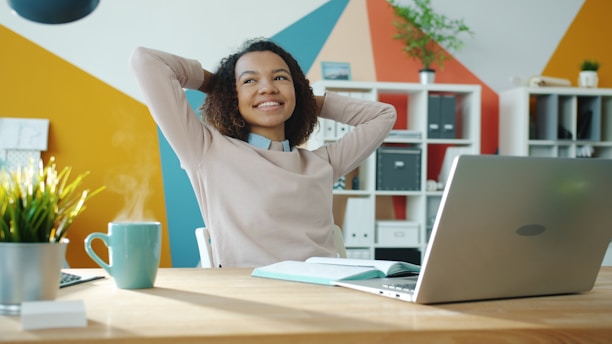 Woman relaxing at desk with laptop and coffee.