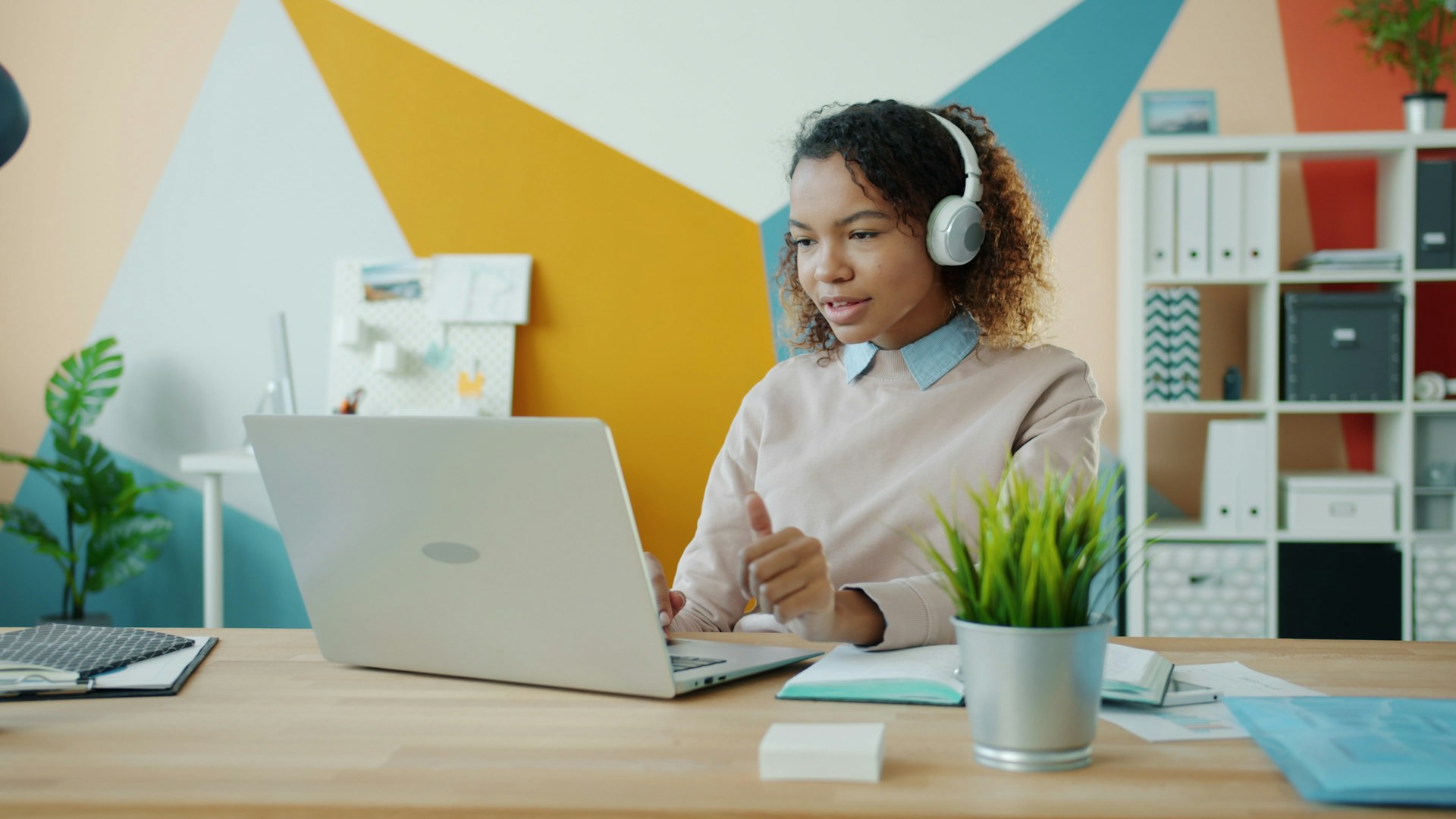 Woman wearing headphones works on a laptop at a desk.