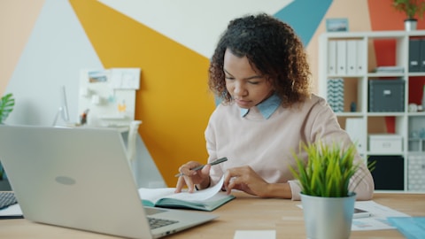 Woman working at a desk with a laptop and notebook.