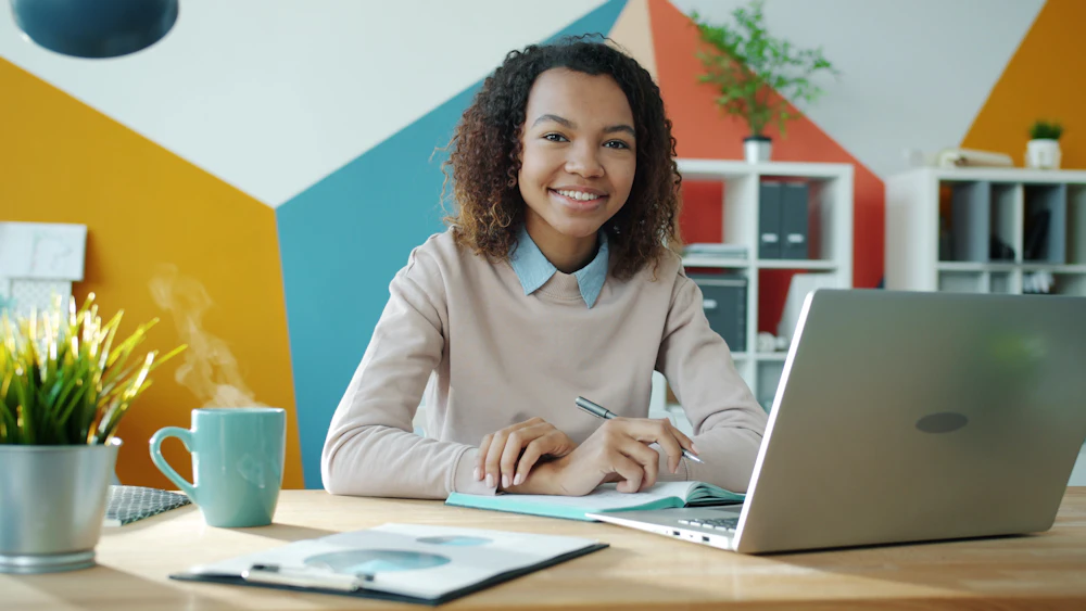 A creator smiling at her desk, reviewing her finished product with a cup of coffee.