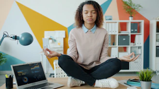 Woman meditating at a desk with laptop.