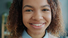 A young woman with curly hair smiles warmly.