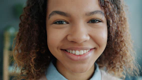 A young woman with curly hair smiles warmly.