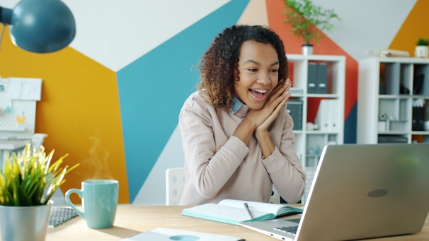 Excited woman looking at laptop with steaming coffee.
