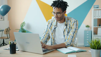 Man working on laptop at desk with colorful wall background.