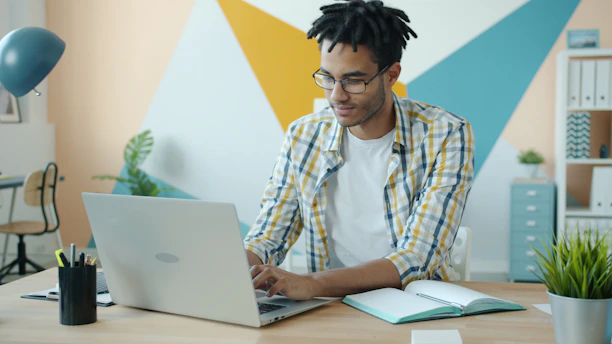 Man working on laptop at desk with colorful wall background.