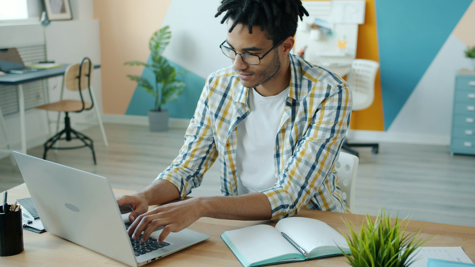 Man typing on laptop at a desk with notebook.