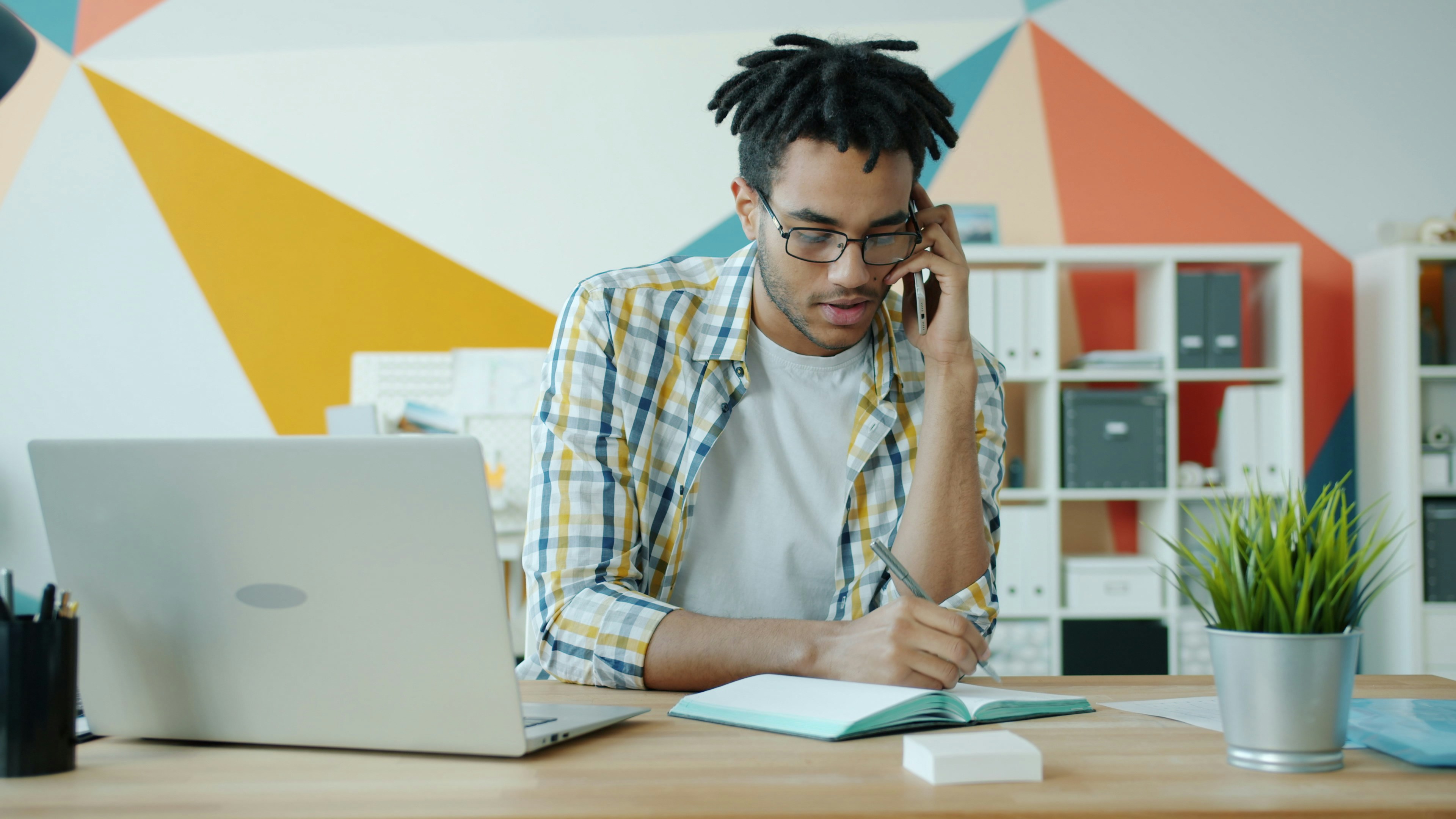 Man talking on phone at a desk with laptop and notebook