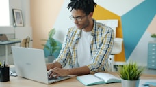 Man with dreadlocks working on a laptop at a desk.