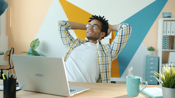 Man relaxing at desk with laptop and coffee.