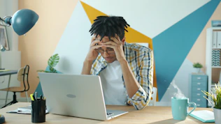 Man holding head in frustration at desk with laptop.