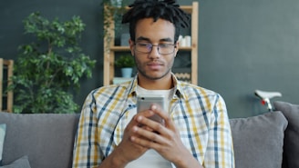 Man with glasses using a smartphone on couch.