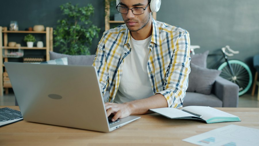 Student with headphones typing on a laptop beside an open notebook