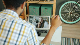 Man video calling two smiling women on laptop.