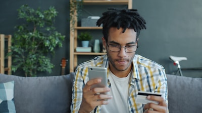 Man holding credit card and smartphone on couch