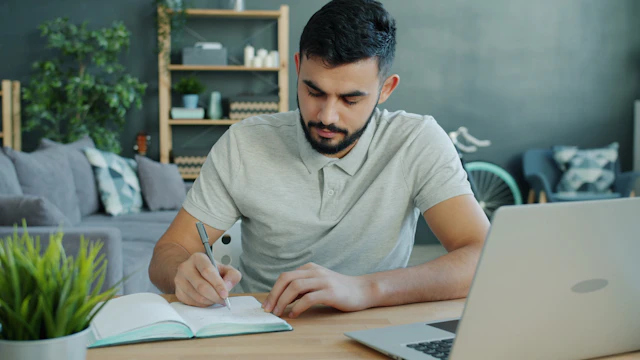 Estudiante tomando apuntes junto a un ordenador portátil