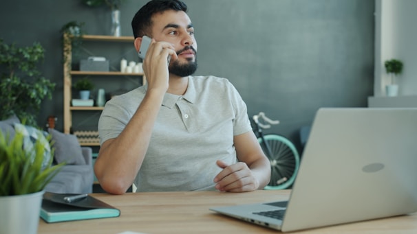 Man talking on phone at desk with laptop.