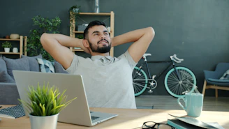 Man relaxing at desk with laptop and bicycle.