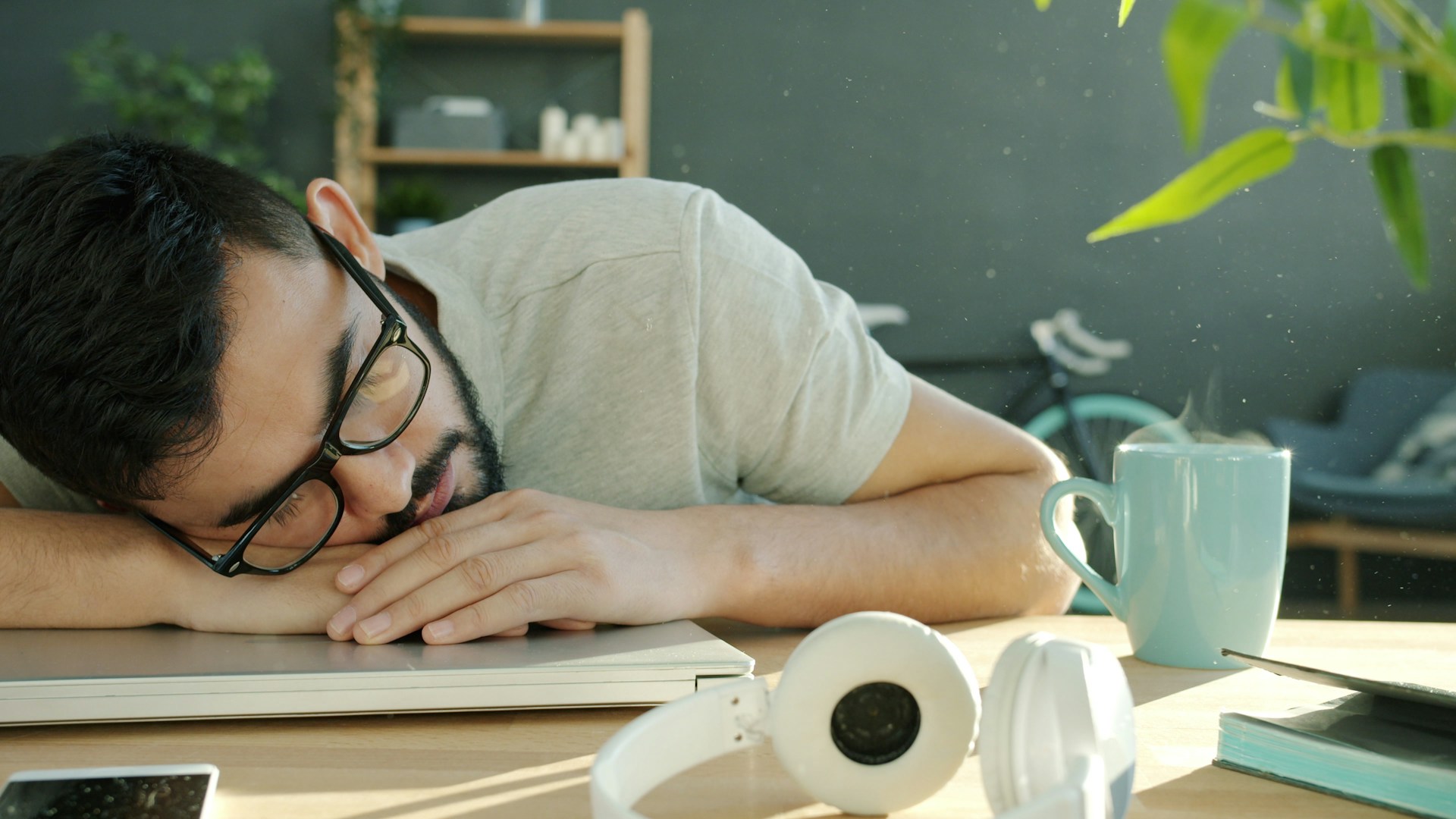 Man sleeping at desk with headphones and coffee.