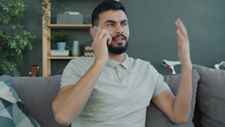 Man talking animatedly on the phone while sitting on couch.