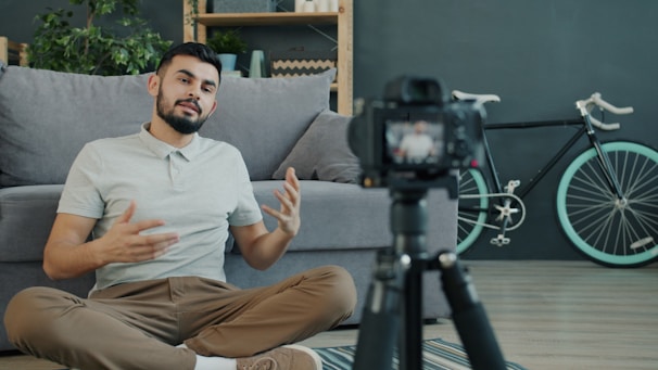 Man sitting on floor talking to camera on tripod.