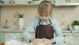 Young girl wearing apron kneading dough in kitchen.