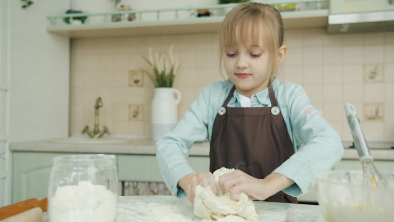 Young girl kneading dough in a kitchen.