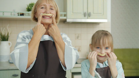 Grandmother and granddaughter making mustache shapes with food.