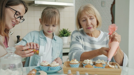 Three women decorating cupcakes in a kitchen.
