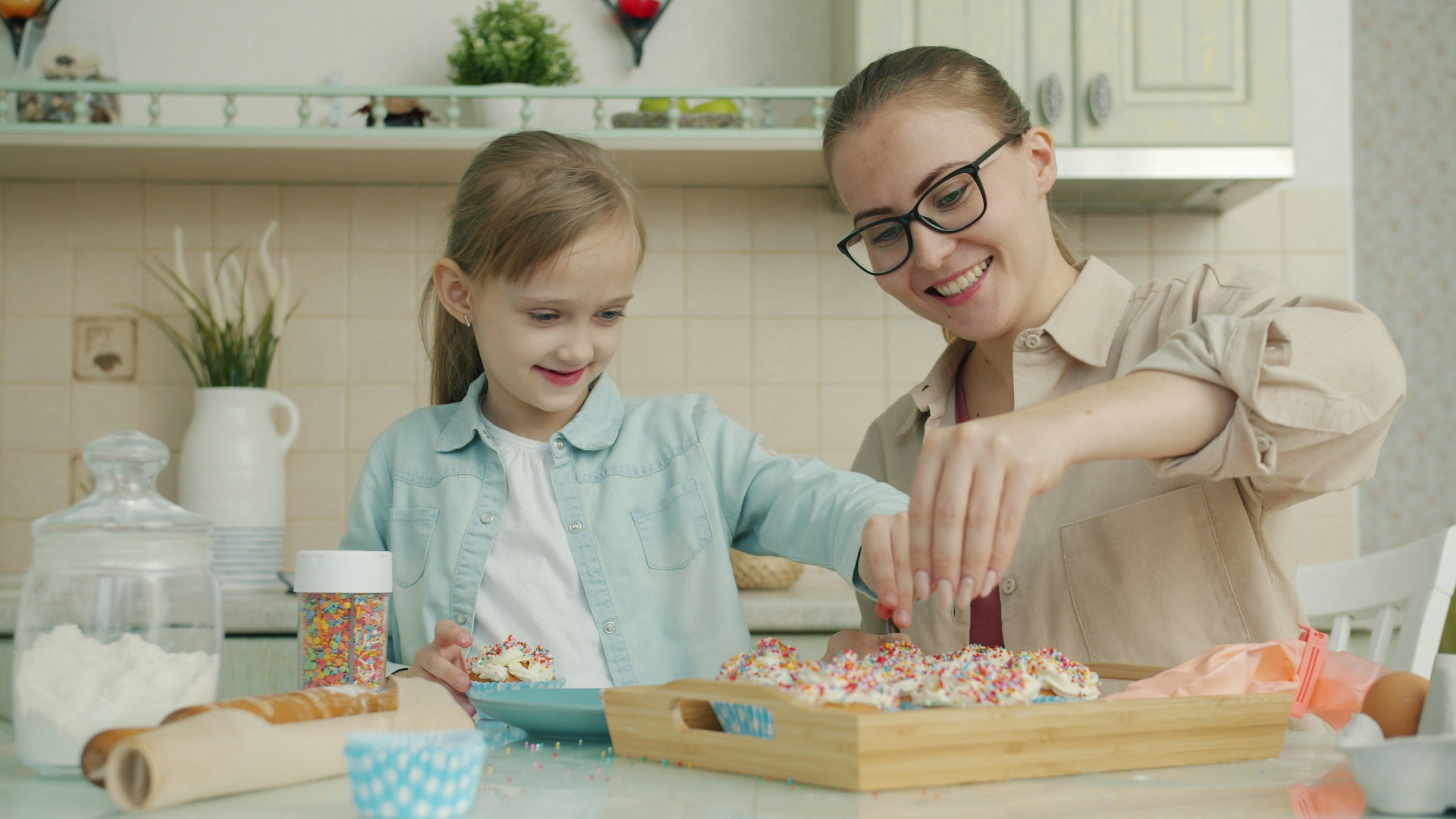 Mother and daughter cheeful people are decorating cupcakes in kitchen discussing food preparation at home. Cookery, childhood and motherhood concept.