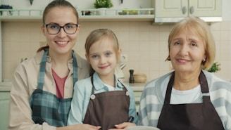 Three smiling women in a kitchen wearing aprons.